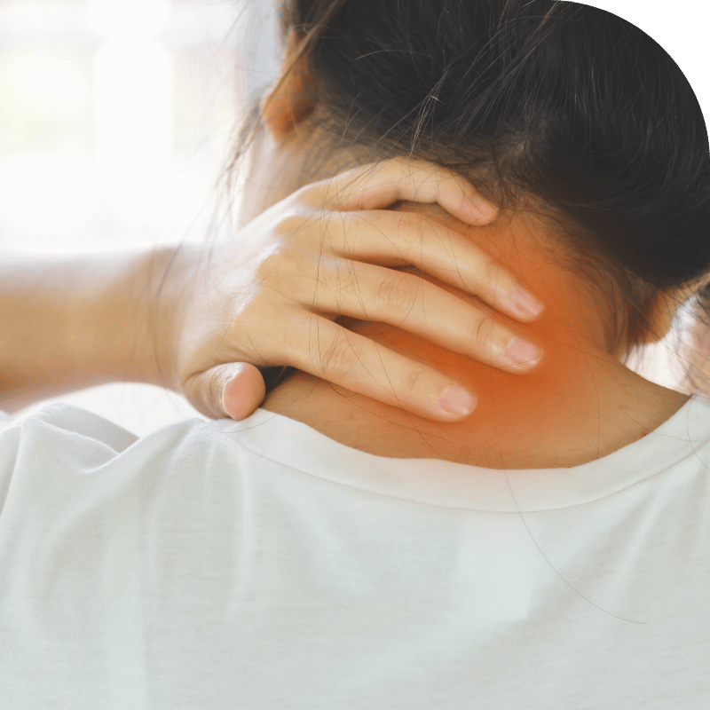A close-up of a person with dark hair wearing a white shirt, holding the back of their neck with both hands. The area around the neck is highlighted in orange, indicating discomfort or pain. The background is a plain white wall with a green section at the top.